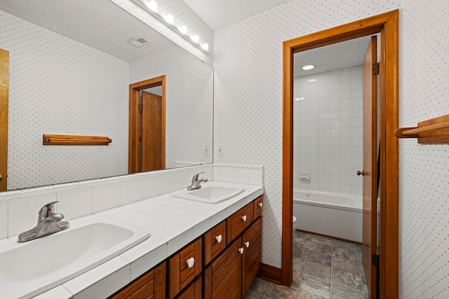 full bathroom with vanity, tiled shower / bath, toilet, and a textured ceiling