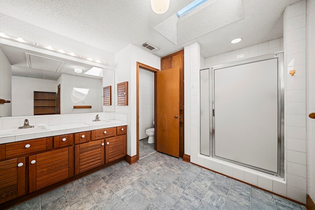 bathroom featuring toilet, vanity, a textured ceiling, and a shower with shower door