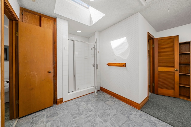 interior space featuring a shower with shower door, a textured ceiling, and a skylight