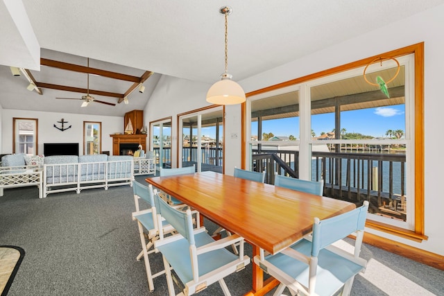 dining area with ceiling fan, vaulted ceiling with beams, a water view, carpet floors, and a fireplace