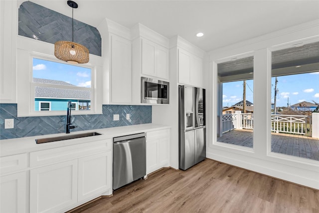 kitchen featuring sink, white cabinetry, decorative light fixtures, light wood-type flooring, and stainless steel appliances