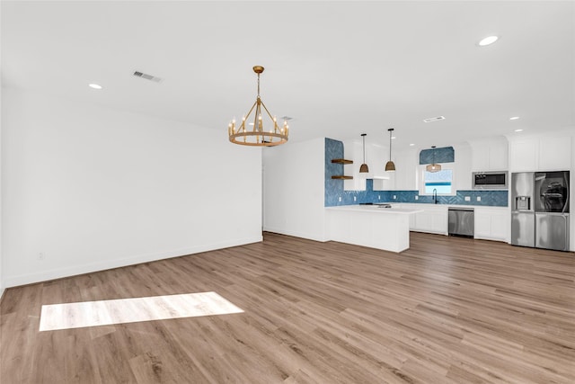 kitchen featuring appliances with stainless steel finishes, white cabinetry, sink, hanging light fixtures, and light wood-type flooring