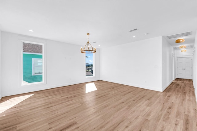 unfurnished room with a chandelier and light wood-type flooring