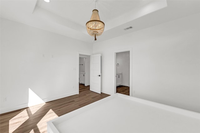 bedroom with dark hardwood / wood-style flooring, a notable chandelier, ensuite bath, and a raised ceiling