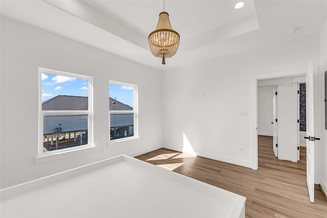 unfurnished bedroom with hardwood / wood-style flooring, a raised ceiling, and a chandelier