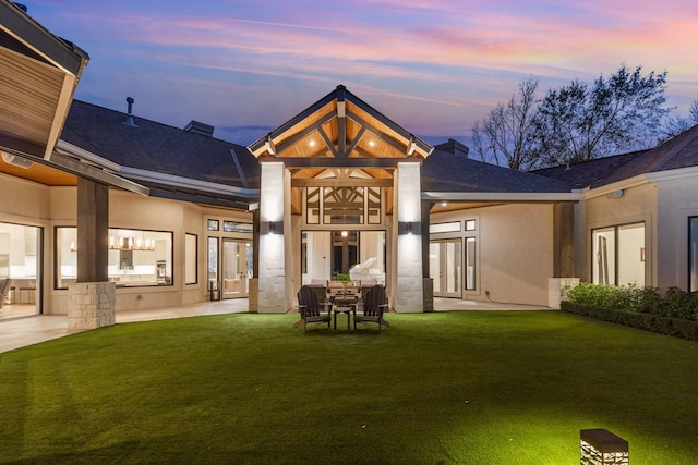 back house at dusk with a patio and a lawn