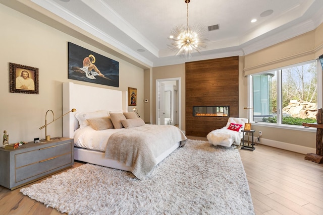 bedroom featuring a fireplace, a chandelier, ornamental molding, light hardwood / wood-style floors, and a raised ceiling