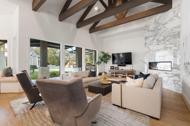 living room with beamed ceiling, a large fireplace, high vaulted ceiling, and light hardwood / wood-style flooring