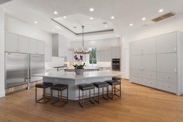 kitchen featuring decorative light fixtures, a breakfast bar area, high end appliances, a raised ceiling, and a spacious island