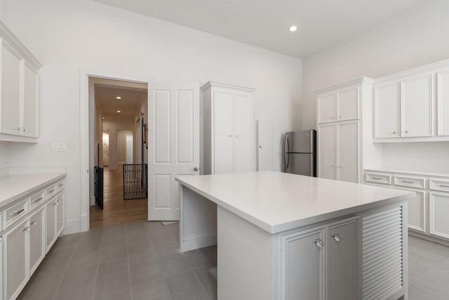 kitchen with tile patterned floors, stainless steel fridge, a kitchen island, and white cabinets