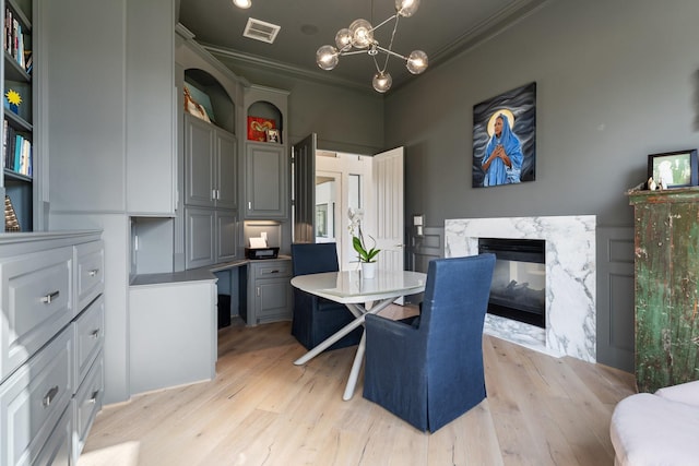 dining room with crown molding, a notable chandelier, a fireplace, and light hardwood / wood-style flooring