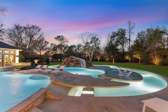 pool at dusk with a water slide, a patio area, and a lawn