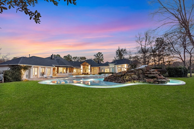 back house at dusk featuring a lawn