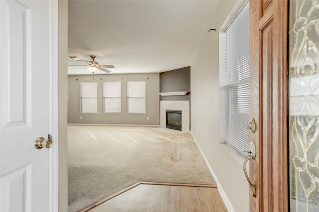 unfurnished living room featuring light carpet, a tiled fireplace, and ceiling fan