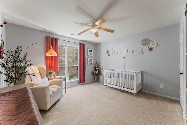 carpeted bedroom featuring ceiling fan, a crib, and a textured ceiling