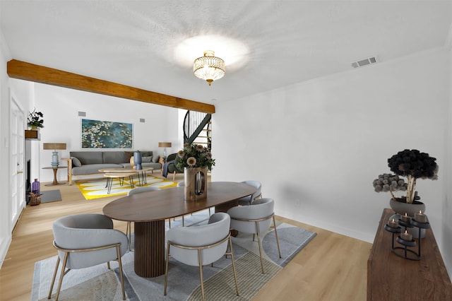 dining area with light wood-type flooring, beamed ceiling, and a notable chandelier