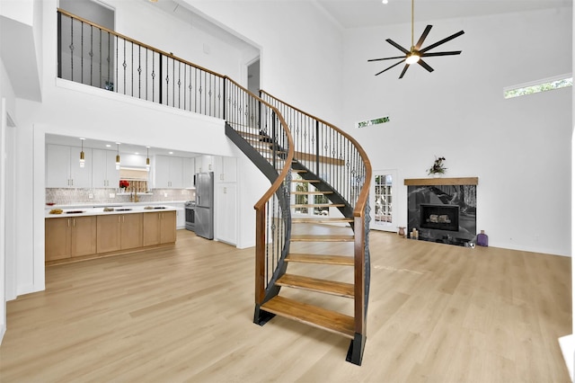 staircase with a premium fireplace, a towering ceiling, ceiling fan, and hardwood / wood-style floors