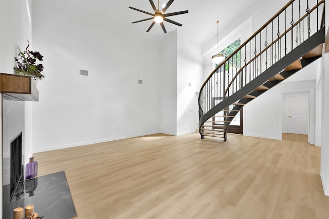 unfurnished living room featuring ceiling fan, light hardwood / wood-style flooring, and a towering ceiling