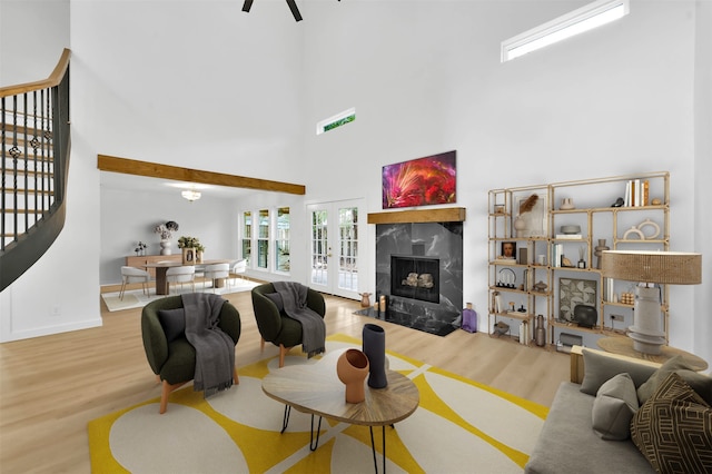 living room with wood-type flooring, a towering ceiling, a fireplace, and french doors