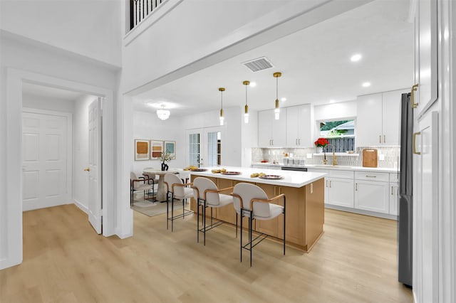 kitchen with white cabinets, a center island, decorative light fixtures, decorative backsplash, and a kitchen breakfast bar