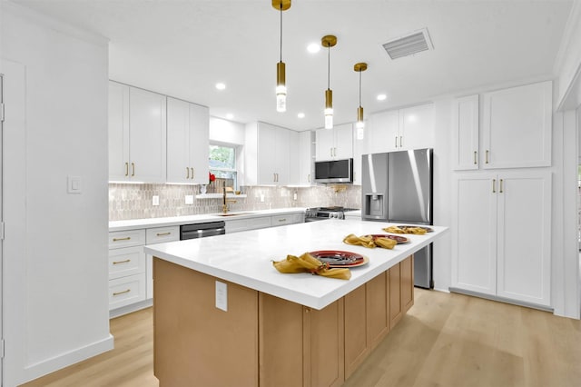 kitchen featuring hanging light fixtures, appliances with stainless steel finishes, sink, white cabinetry, and a kitchen island