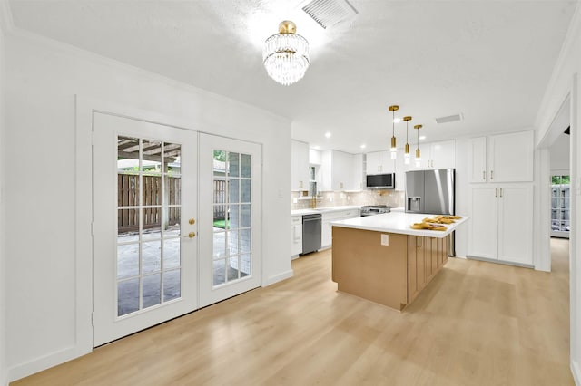 kitchen with light hardwood / wood-style floors, appliances with stainless steel finishes, white cabinets, a kitchen island, and decorative light fixtures