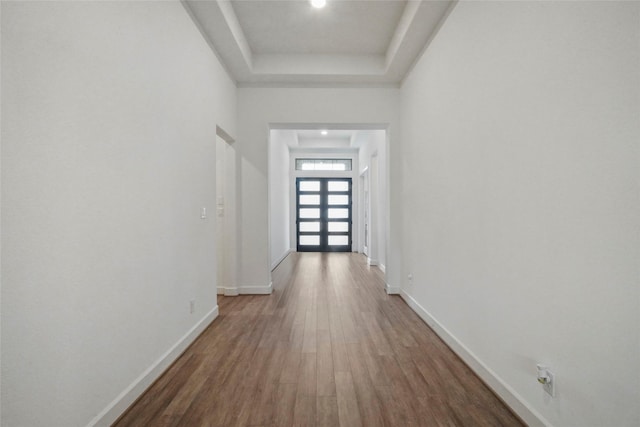 hall with a raised ceiling, dark wood-type flooring, and a towering ceiling