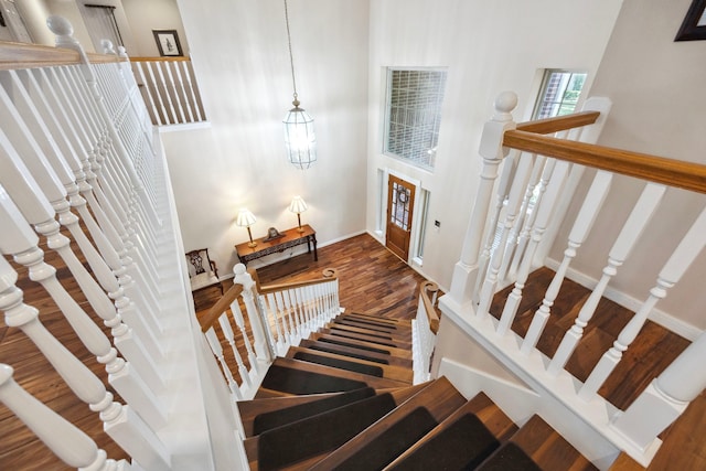 staircase with a high ceiling, hardwood / wood-style floors, and a notable chandelier