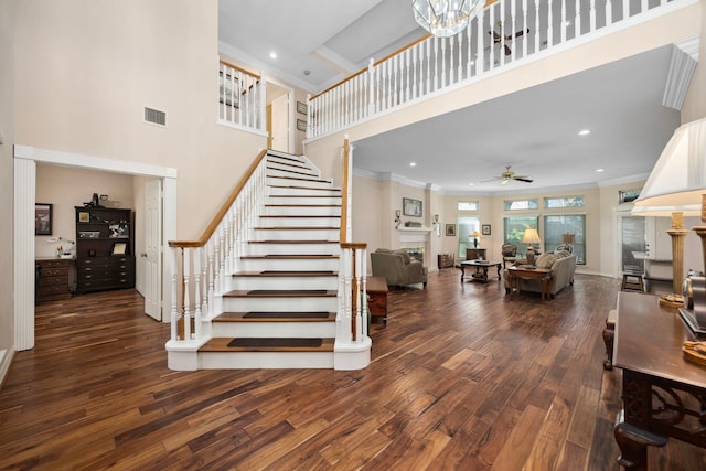 staircase featuring hardwood / wood-style flooring, crown molding, a high ceiling, and ceiling fan with notable chandelier