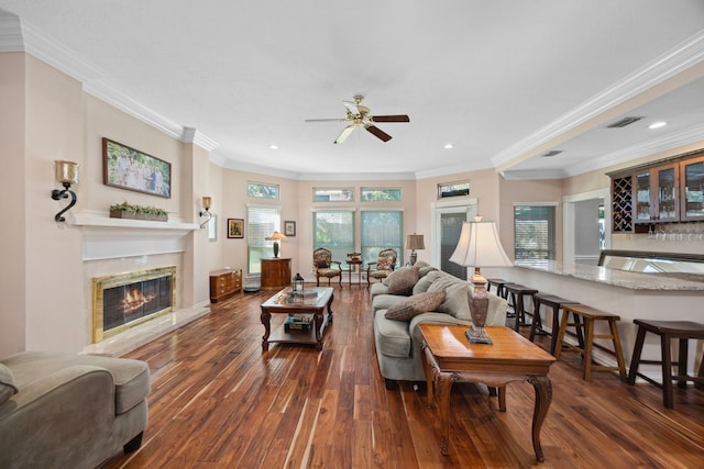 living room featuring bar area, ornamental molding, dark hardwood / wood-style flooring, ceiling fan, and a fireplace