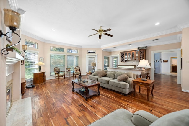 living room featuring bar, crown molding, wood-type flooring, ceiling fan, and a fireplace