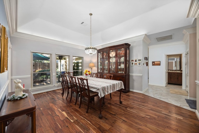 dining area with a raised ceiling, ornamental molding, dark wood-type flooring, and a chandelier