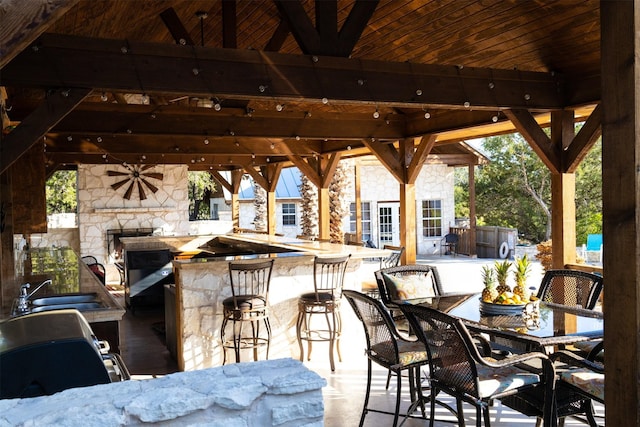 view of patio with ceiling fan, a gazebo, an outdoor stone fireplace, and an outdoor wet bar