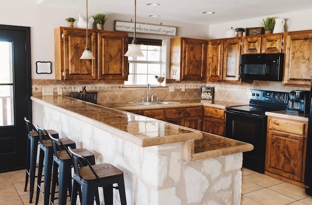 kitchen featuring black appliances, a kitchen bar, decorative light fixtures, sink, and kitchen peninsula