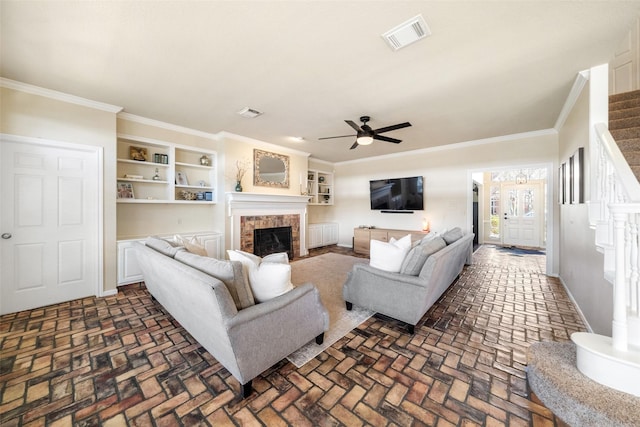 living room featuring crown molding, ceiling fan, built in shelves, and a brick fireplace