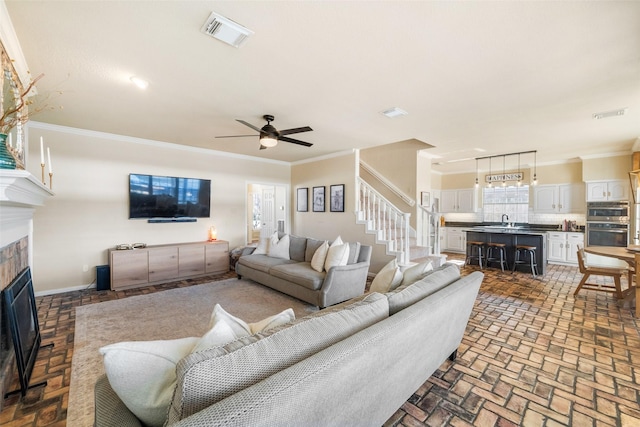 living room featuring crown molding, ceiling fan, sink, and a tile fireplace