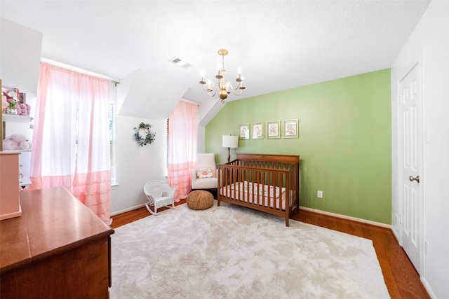 bedroom with hardwood / wood-style flooring, a chandelier, and a crib