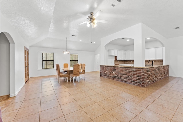 tiled dining room featuring ceiling fan with notable chandelier, sink, vaulted ceiling, and a textured ceiling