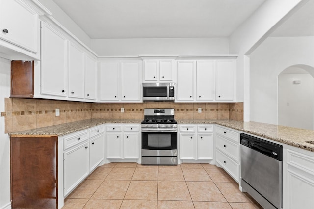 kitchen featuring light tile patterned floors, appliances with stainless steel finishes, backsplash, light stone counters, and white cabinets