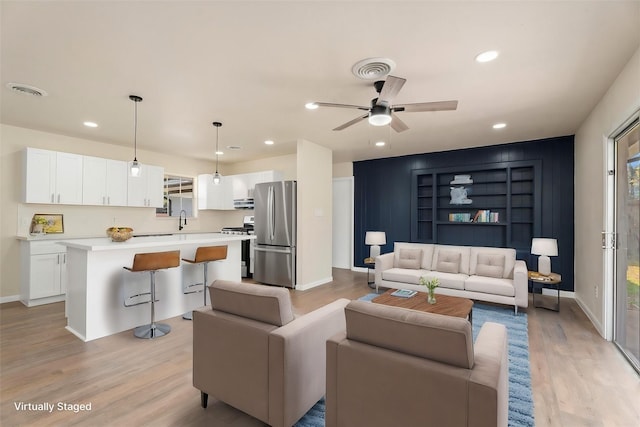 living room featuring sink, built in shelves, ceiling fan, and light hardwood / wood-style floors