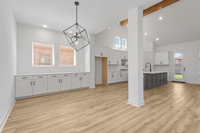 kitchen with pendant lighting, white cabinetry, beam ceiling, tasteful backsplash, and light hardwood / wood-style floors