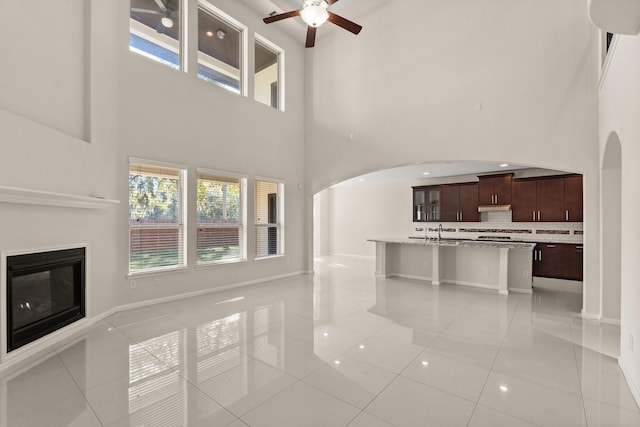 unfurnished living room featuring ceiling fan, a high ceiling, sink, and light tile patterned flooring