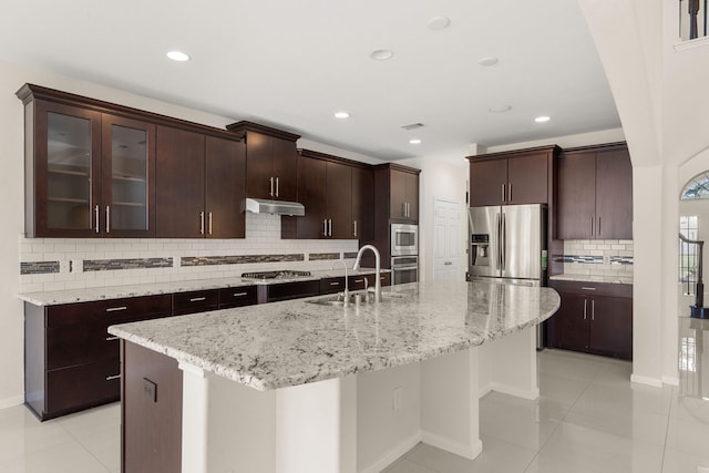 kitchen featuring appliances with stainless steel finishes, sink, light tile patterned floors, a kitchen island with sink, and dark brown cabinetry