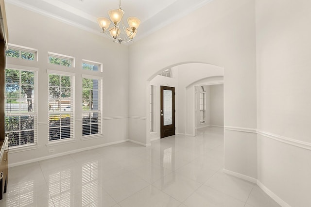 tiled spare room featuring an inviting chandelier, a high ceiling, and ornamental molding