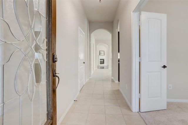 hallway featuring light tile patterned floors, arched walkways, and baseboards