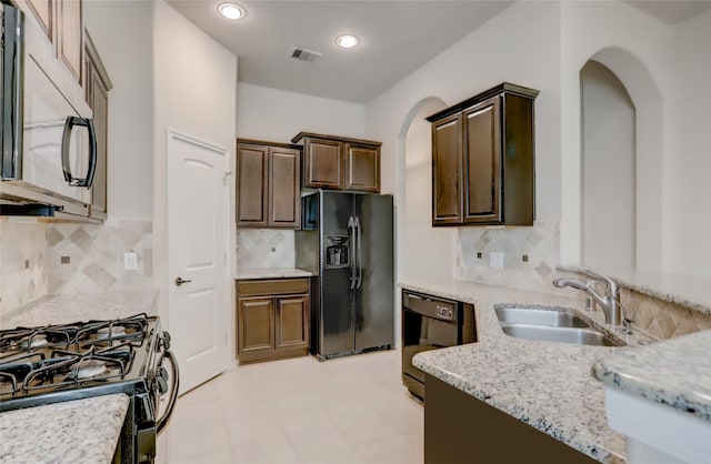 kitchen featuring black appliances, decorative backsplash, sink, dark brown cabinetry, and light stone counters