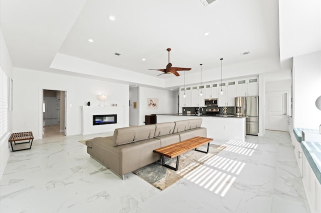 living room featuring ceiling fan, sink, and a raised ceiling