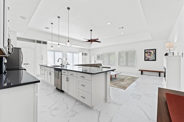 kitchen featuring white cabinets, appliances with stainless steel finishes, decorative light fixtures, an island with sink, and a tray ceiling