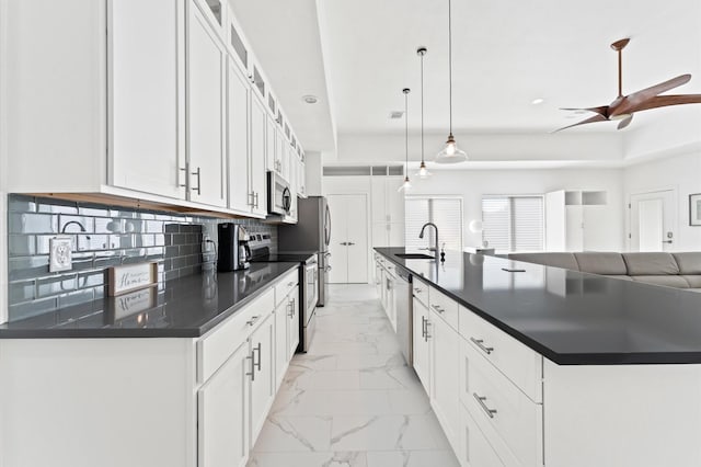 kitchen with stainless steel appliances, decorative light fixtures, white cabinetry, and an island with sink