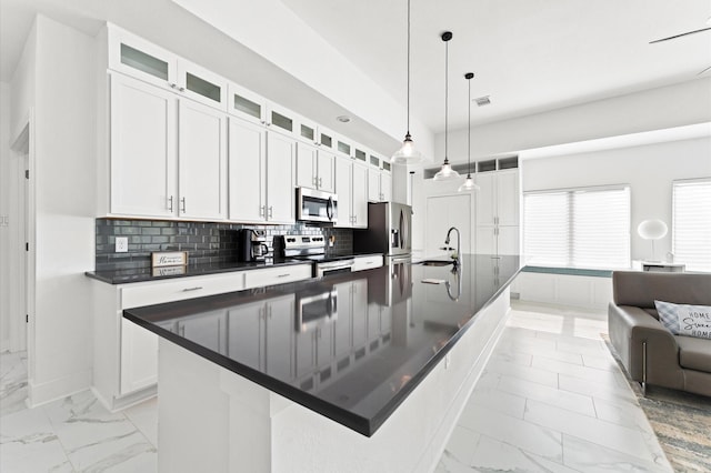 kitchen with appliances with stainless steel finishes, white cabinetry, an island with sink, sink, and hanging light fixtures